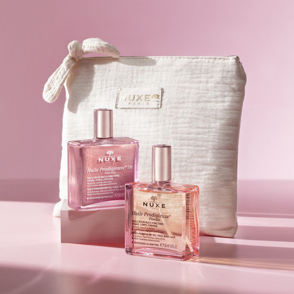 Due flaconi con liquido rosa e dorato, accanto a una pochette beige. Scritta: Nuxe.