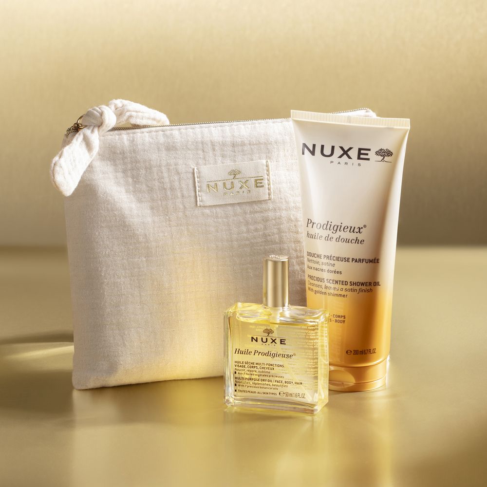 Prodotti Nuxe: gel doccia e olio in una pochette beige. Logo Nuxe e nomi dei prodotti visibili.