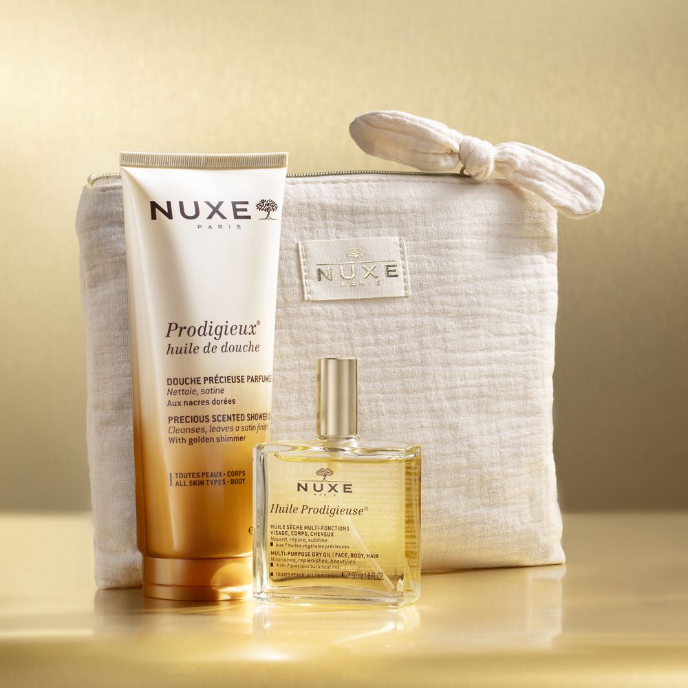 Prodotti Nuxe: gel doccia e olio in una pochette beige. Logo Nuxe e nomi dei prodotti visibili.