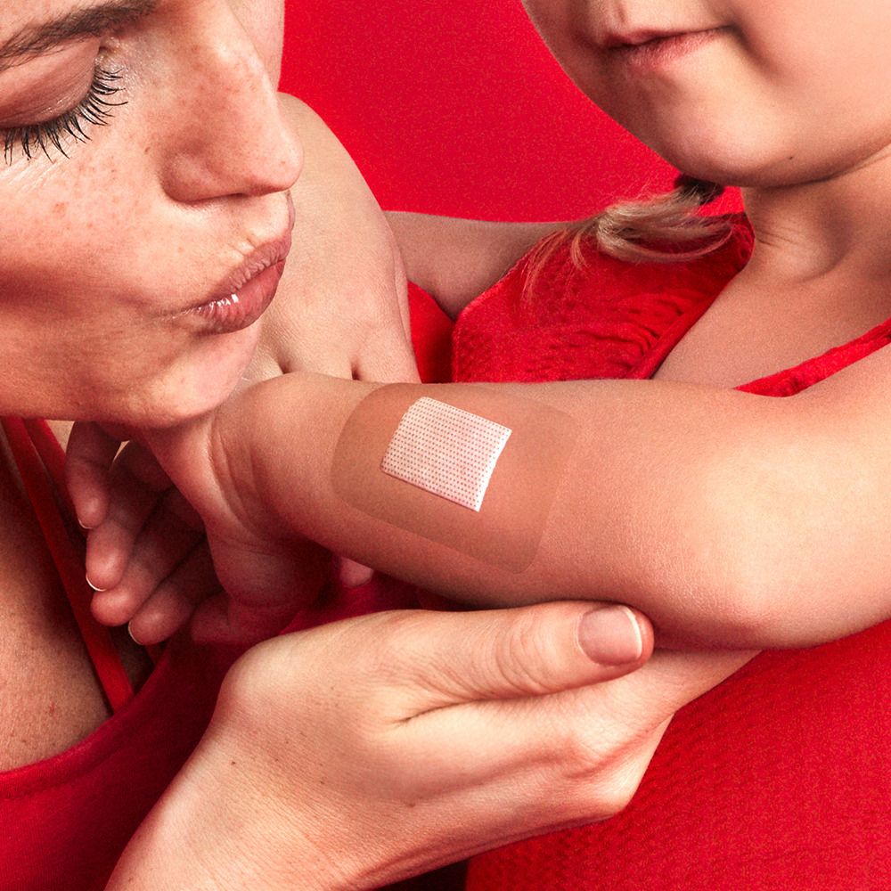 Braccio con cerotto. Madre applica cerotto a bambino. Sfondo rosso.