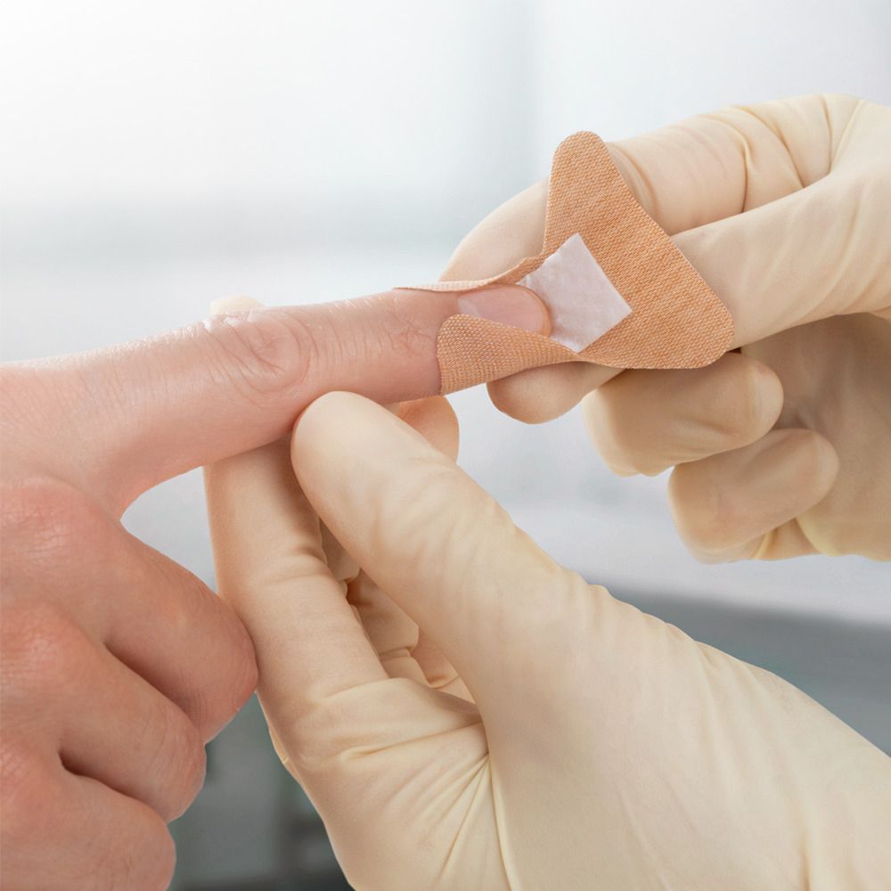 Persona applica cerotto su dito. Cerotto beige con tampone.