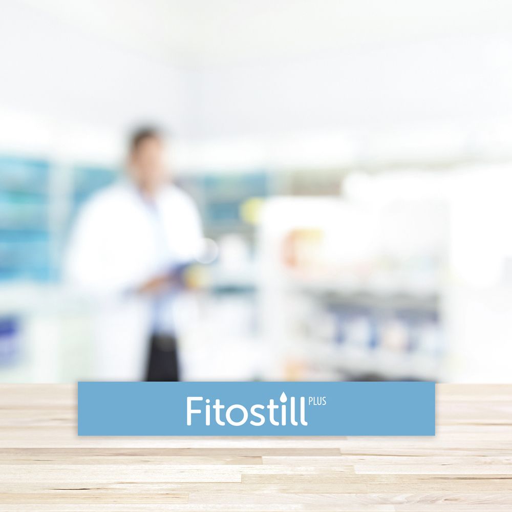 Rettangolo blu con il nome del prodotto 'Fitostill Plus'. Sfondo sfocato.