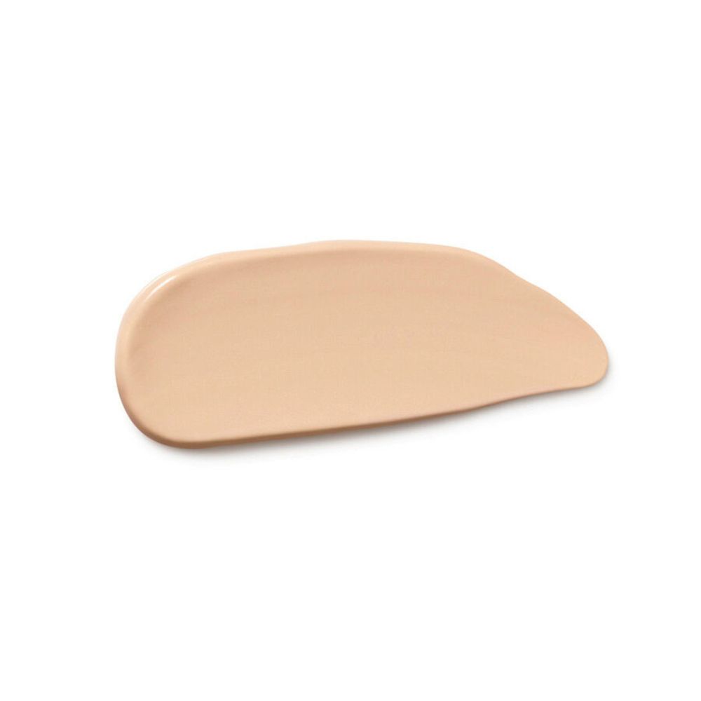 Striscio di correttore marrone chiaro su sfondo bianco. Texture liscia e cremosa.