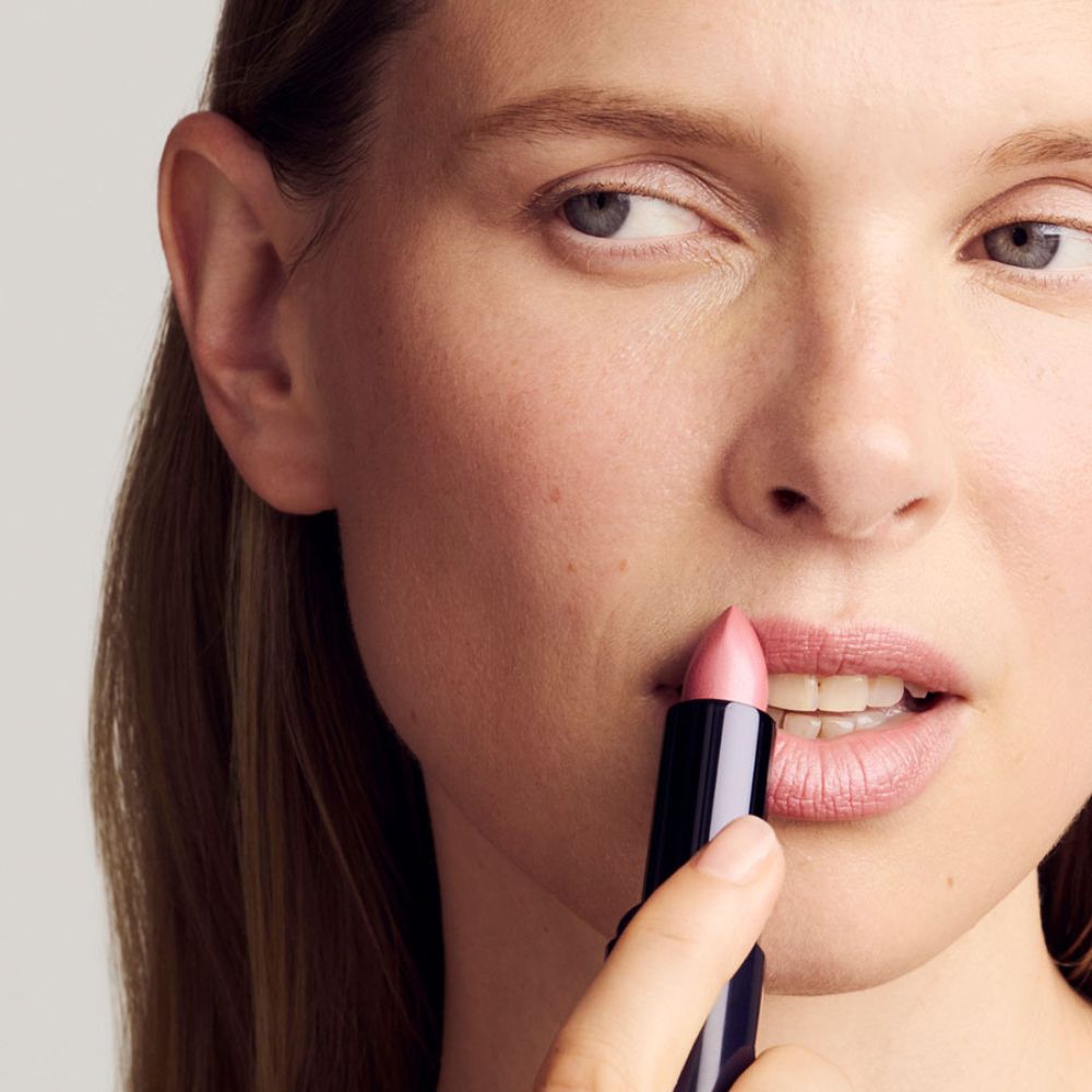 Donna applica rossetto rosa. Rossetto nero in mano.