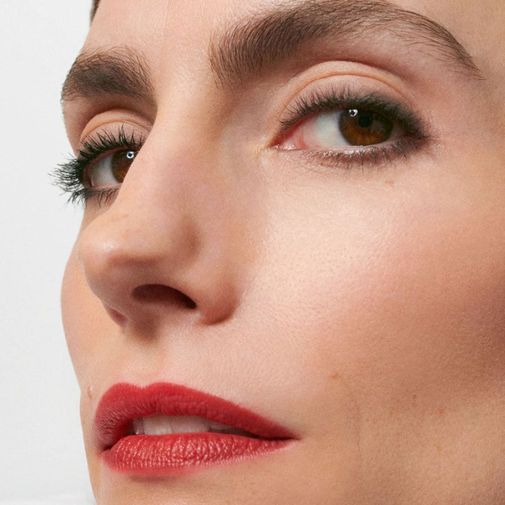 Primo piano di un viso con rossetto rosso. Sopracciglia, occhi e pelle visibili.