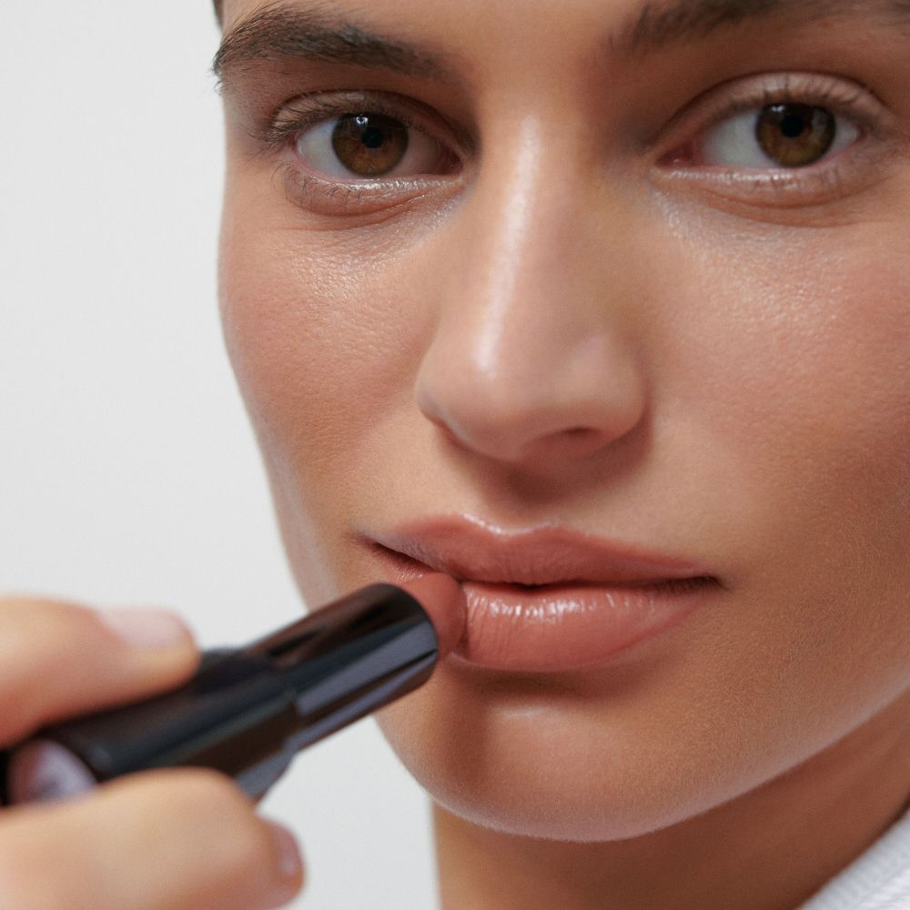 Persona applica rossetto. Rossetto in astuccio nero. Tonalità della pelle. Primo piano.