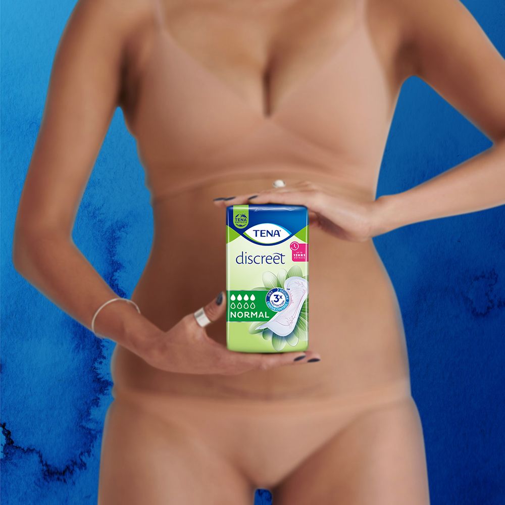 Donna tiene una confezione di Tena Discreet Normal. Prodotto davanti al corpo. Sfondo blu.