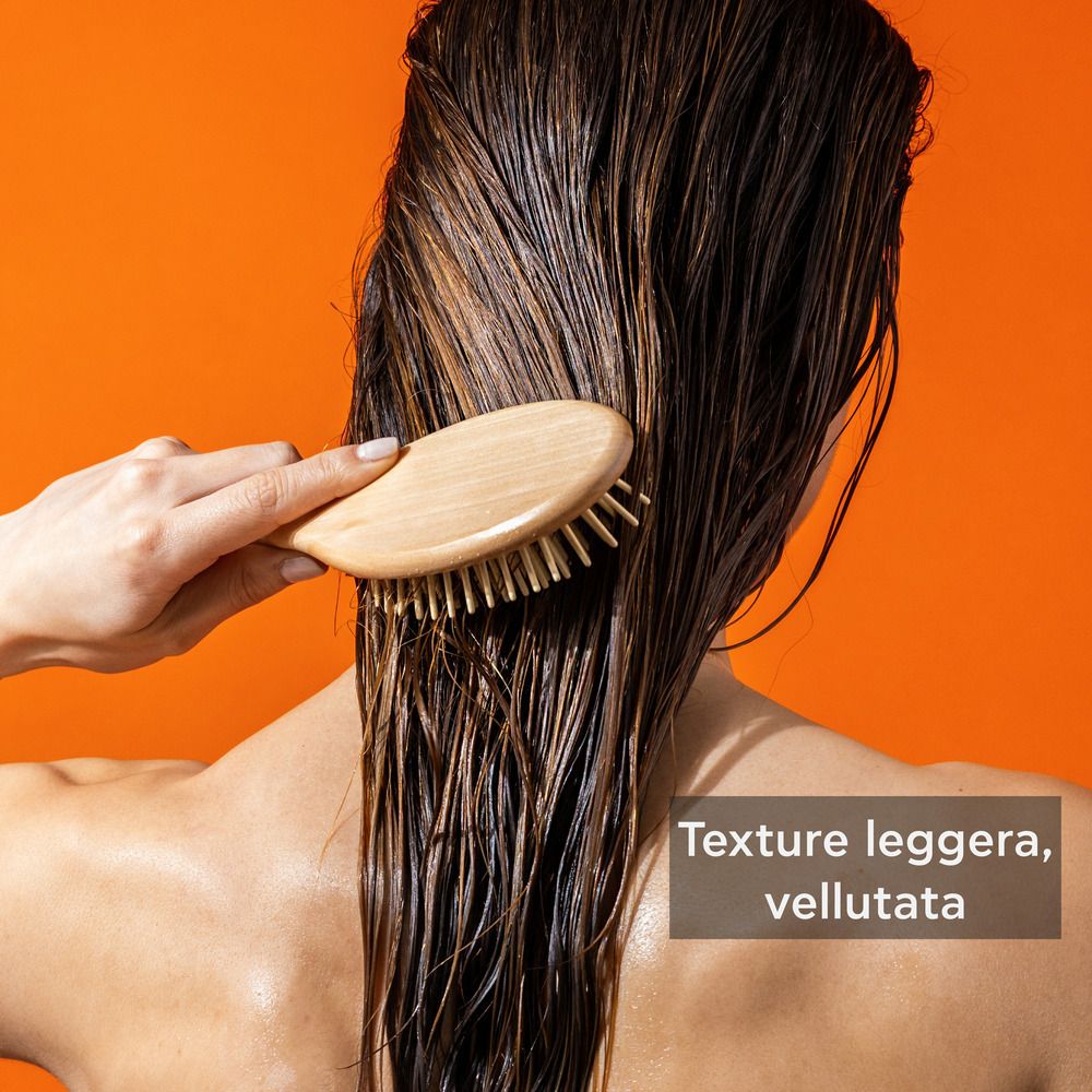 Persona che spazzola i capelli bagnati con una spazzola di legno. Testo: Texture leggera, vellutata.