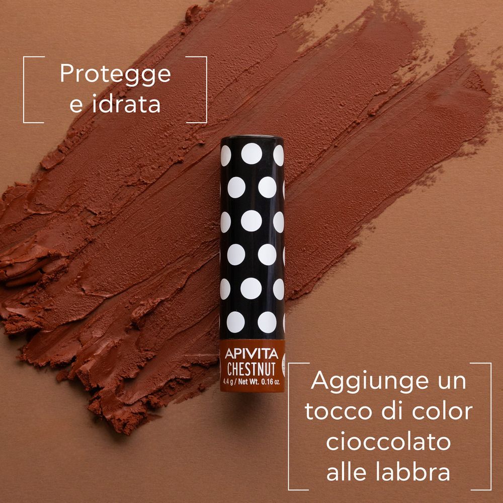Balsamo labbra con astuccio nero a pois. Tracce di rossetto marrone. Testo: APIVITA CHESTNUT. Aggiunge colore.