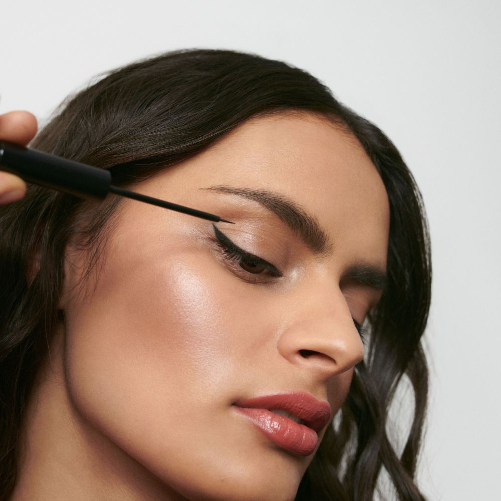 Donna che applica l'eyeliner nero sulla palpebra. Pennello in mano.