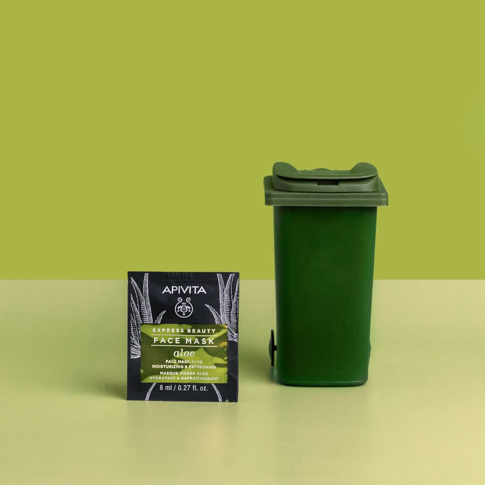 Confezione di maschera viso accanto a un cestino verde. Sfondo verde.