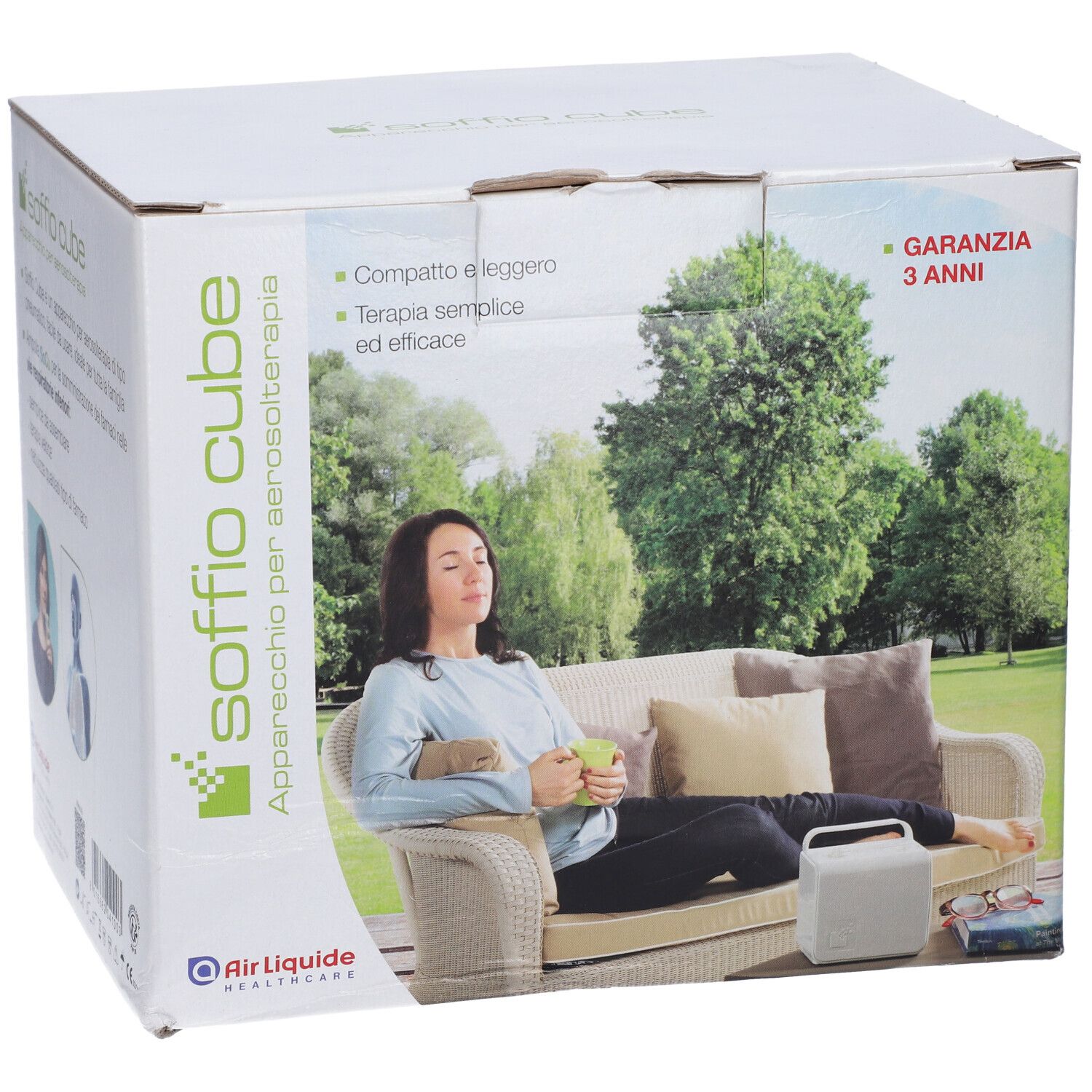 Scatola dell'apparecchio per aerosol Soffio Cube. Scritte: Garanzia 3 anni, Air Liquide Healthcare. Donna su divano con dispositivo.
