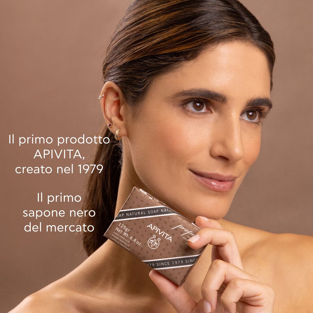 Donna tiene sapone. Testo: Primo prodotto Apivita, creato nel 1979. Primo sapone nero.