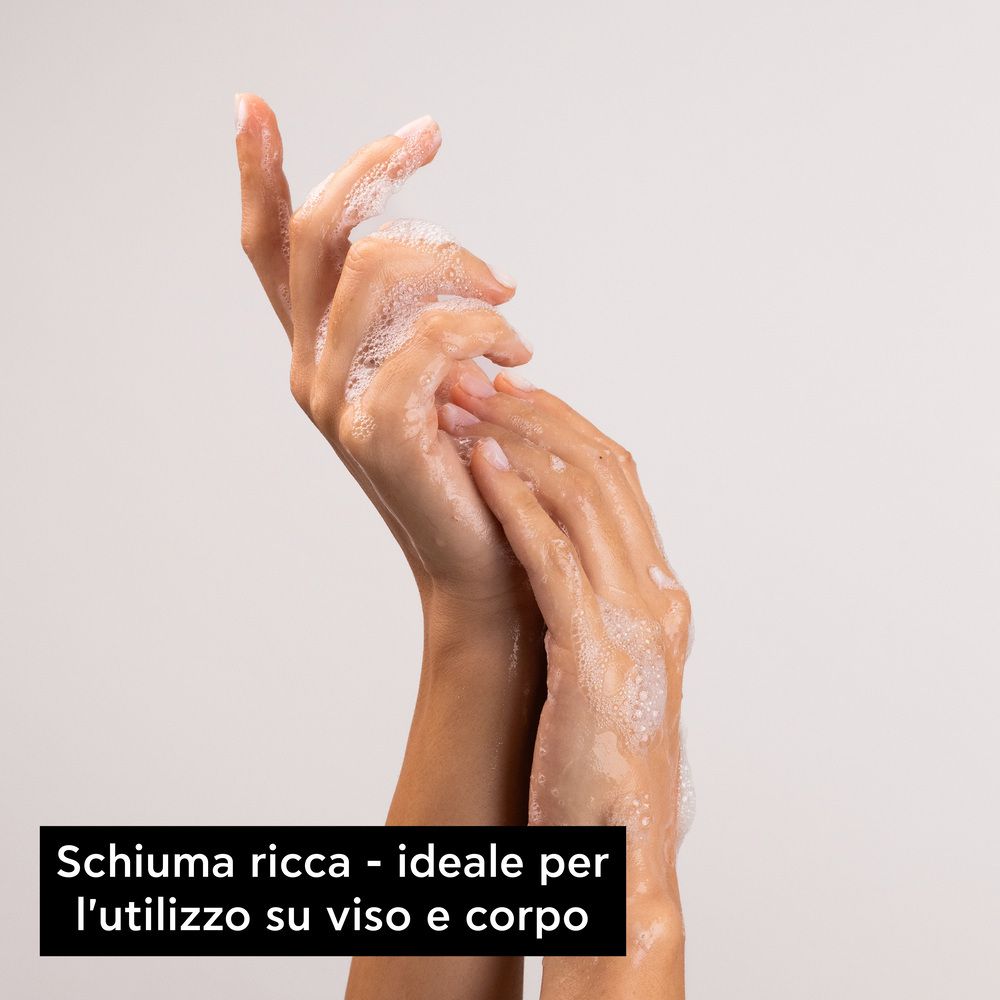 Mani con schiuma di sapone. Testo: Schiuma ricca - ideale per l'utilizzo su viso e corpo.