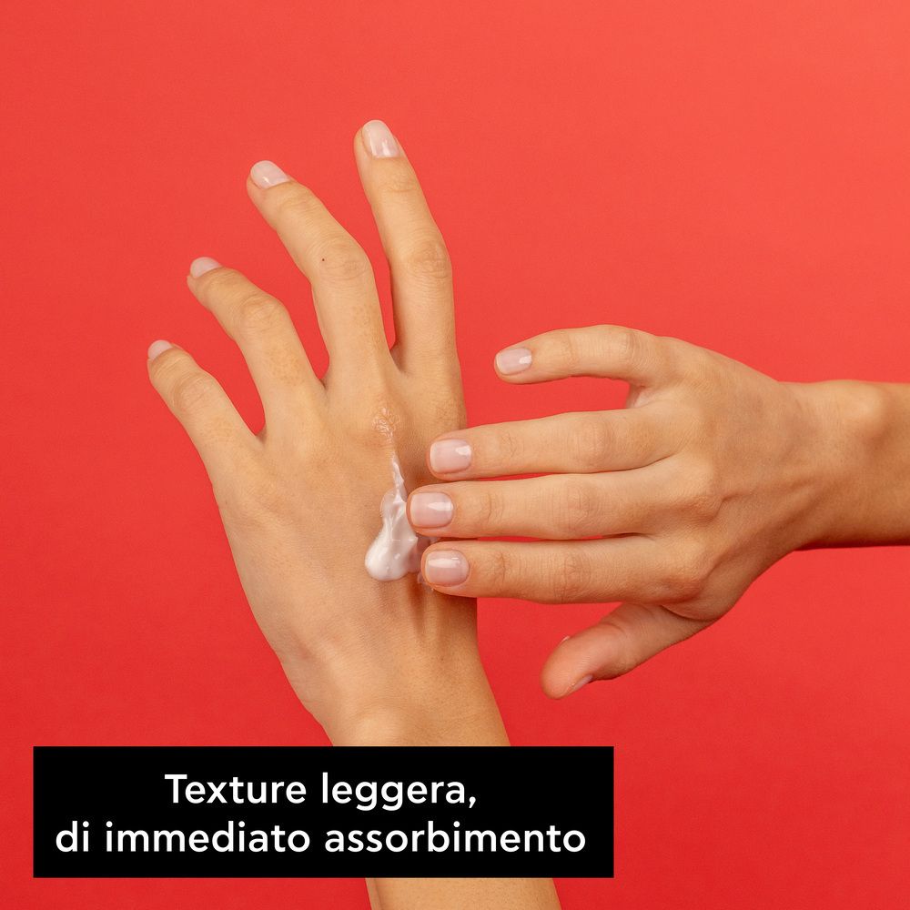 Mani con crema su sfondo rosso. Testo: Texture leggera, di immediato assorbimento.