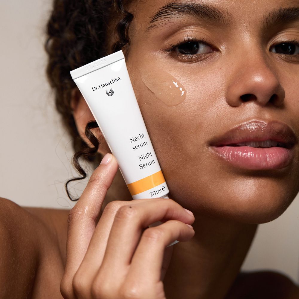 Donna tiene il tubo sulla guancia. Scritta: Nacht Serum. Liquido giallastro sulla pelle.