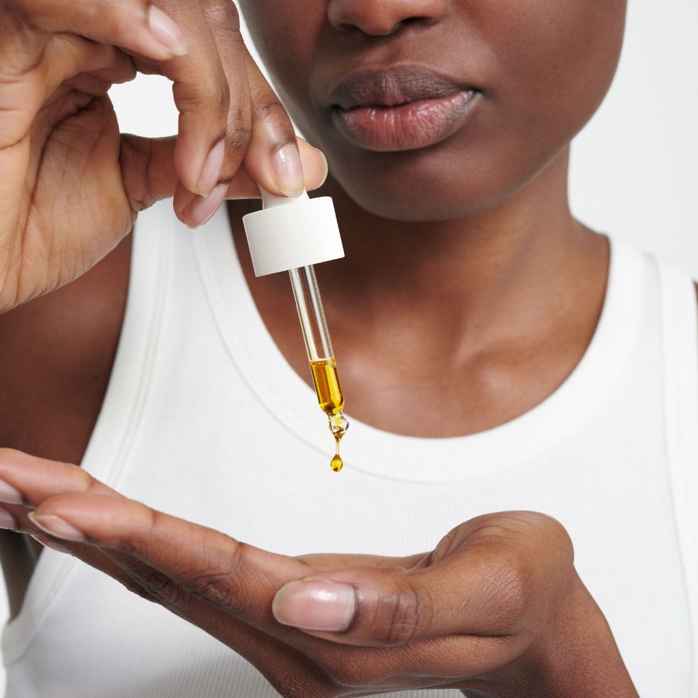 Persona che tiene una pipetta con olio sopra il palmo. L'olio gocciola dalla pipetta.