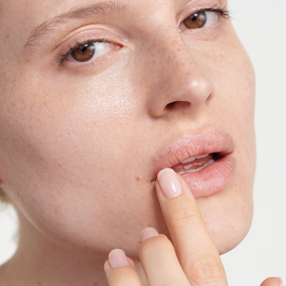Primo piano di labbra a cui viene applicata la crema. Dito che tocca il labbro.