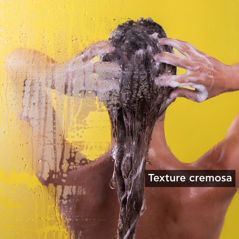 Persona che si lava i capelli con shampoo. Sfondo giallo. Testo: Texture cremosa.