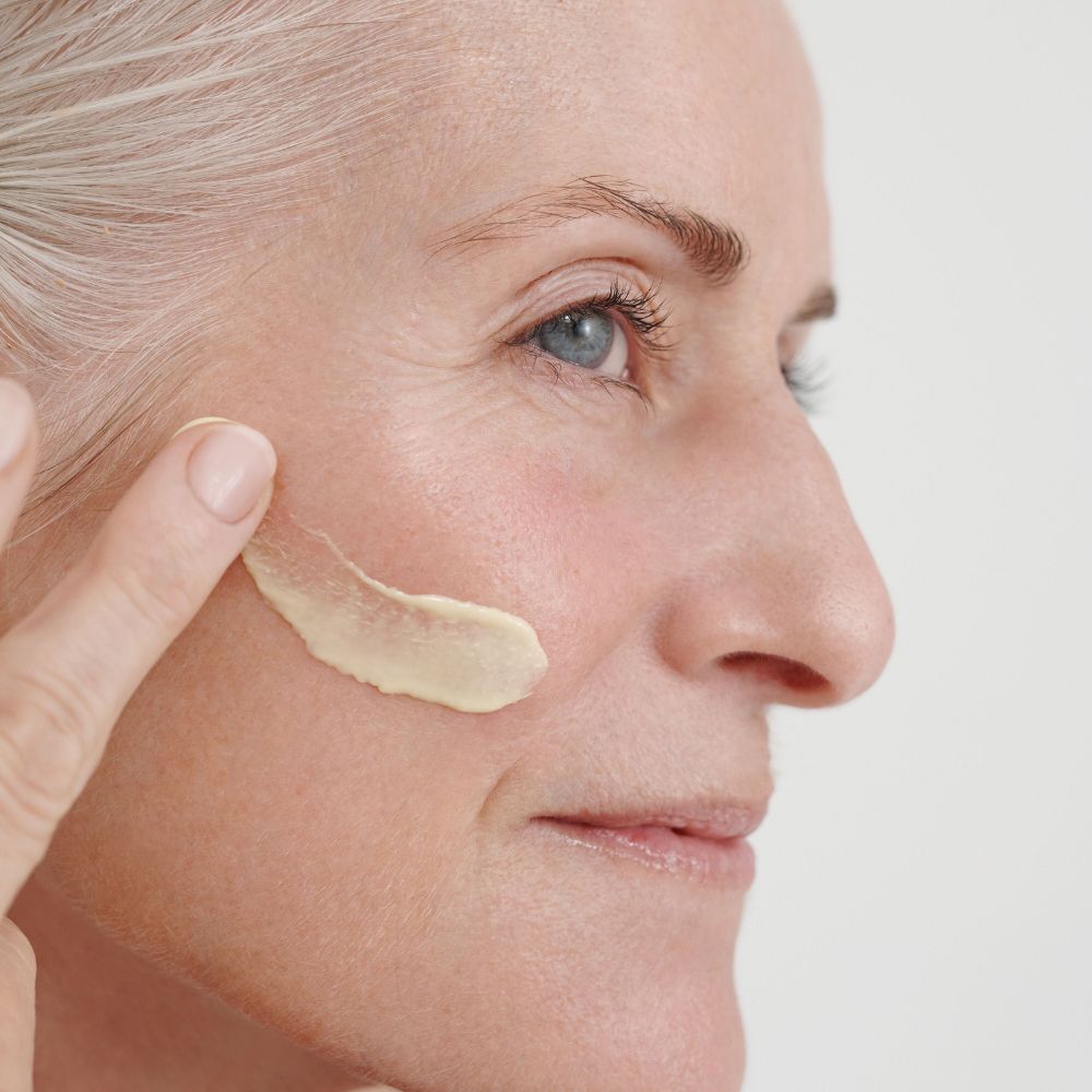 Donna applica crema sulla guancia. La crema è giallastra. La pelle è visibile.