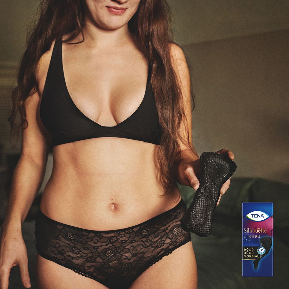 Donna con reggiseno e intimo neri, tiene in mano un proteggislip nero. Piccola confezione sullo sfondo.