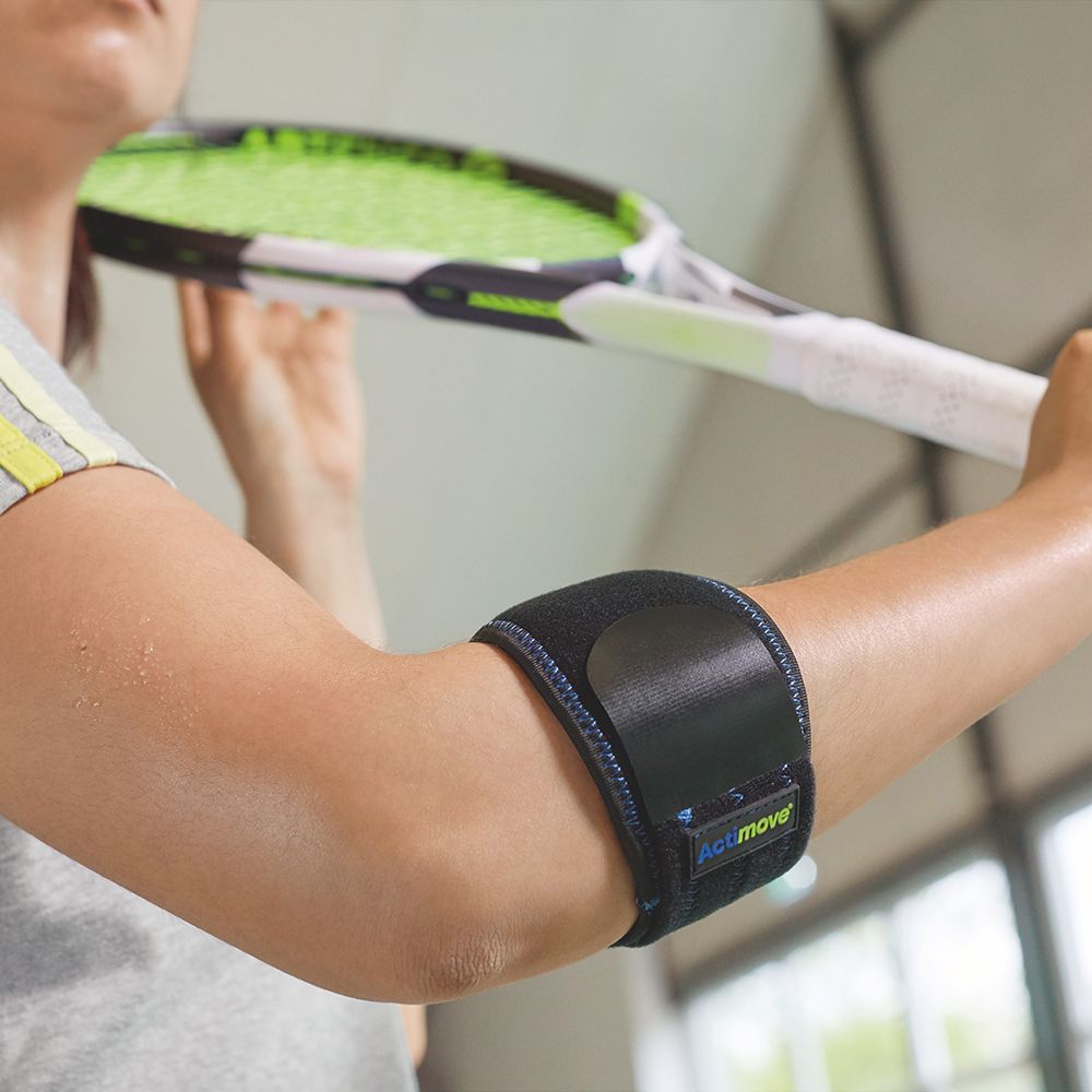 Una donna con fascia per gomito Actimove al braccio. Tiene una racchetta da tennis.