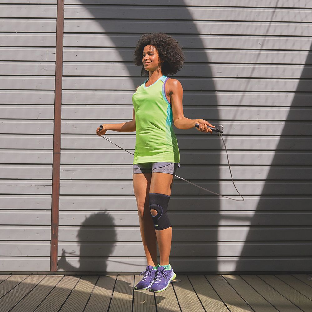 Donna che salta la corda con ginocchiera. Ginocchiera nera sulla gamba sinistra. All'aperto.