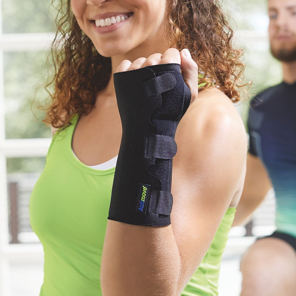 Persona con tutore per polso nero Actimove Sports Edition. Tre chiusure in velcro. Persona in palestra. Canotta verde.