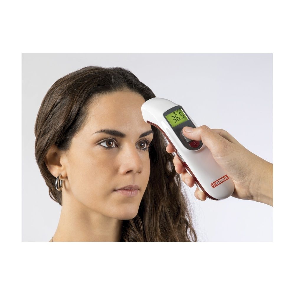 Mano che tiene un termometro senza contatto bianco sulla fronte. Display LCD con temperatura.