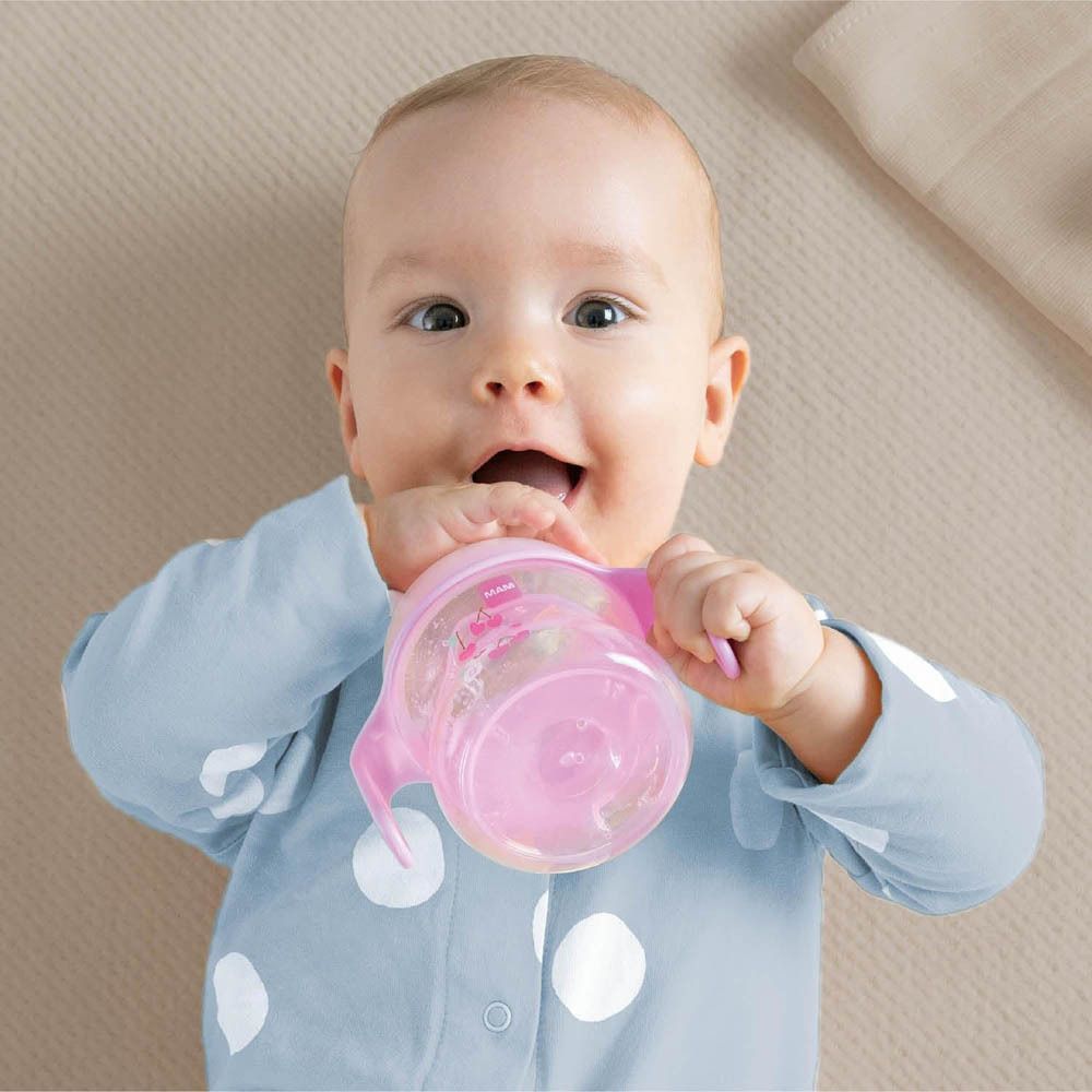 Un bambino tiene una tazza rosa con manici.