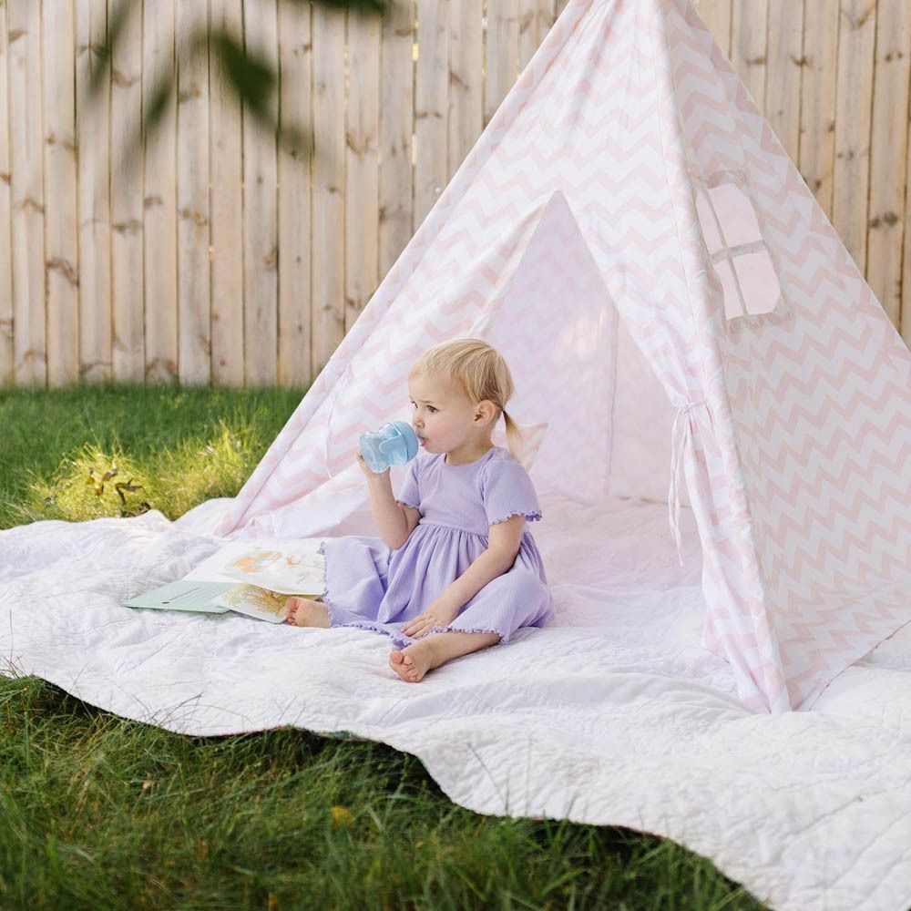 Bambina che beve da una tazza blu all'interno di una tenda da gioco in giardino.