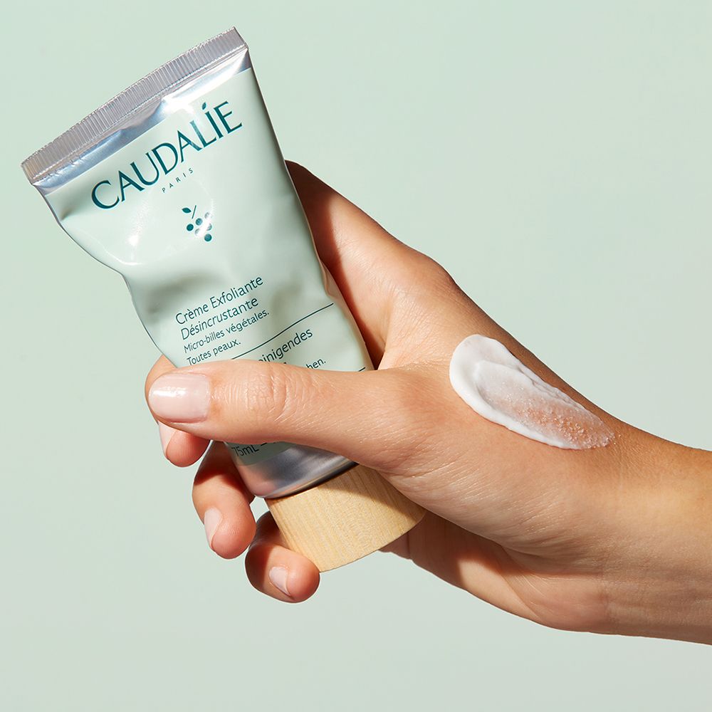 Mano che tiene un tubo di peeling viso CAUDALÍE. Goccia di peeling sulla mano. Tappo in legno.