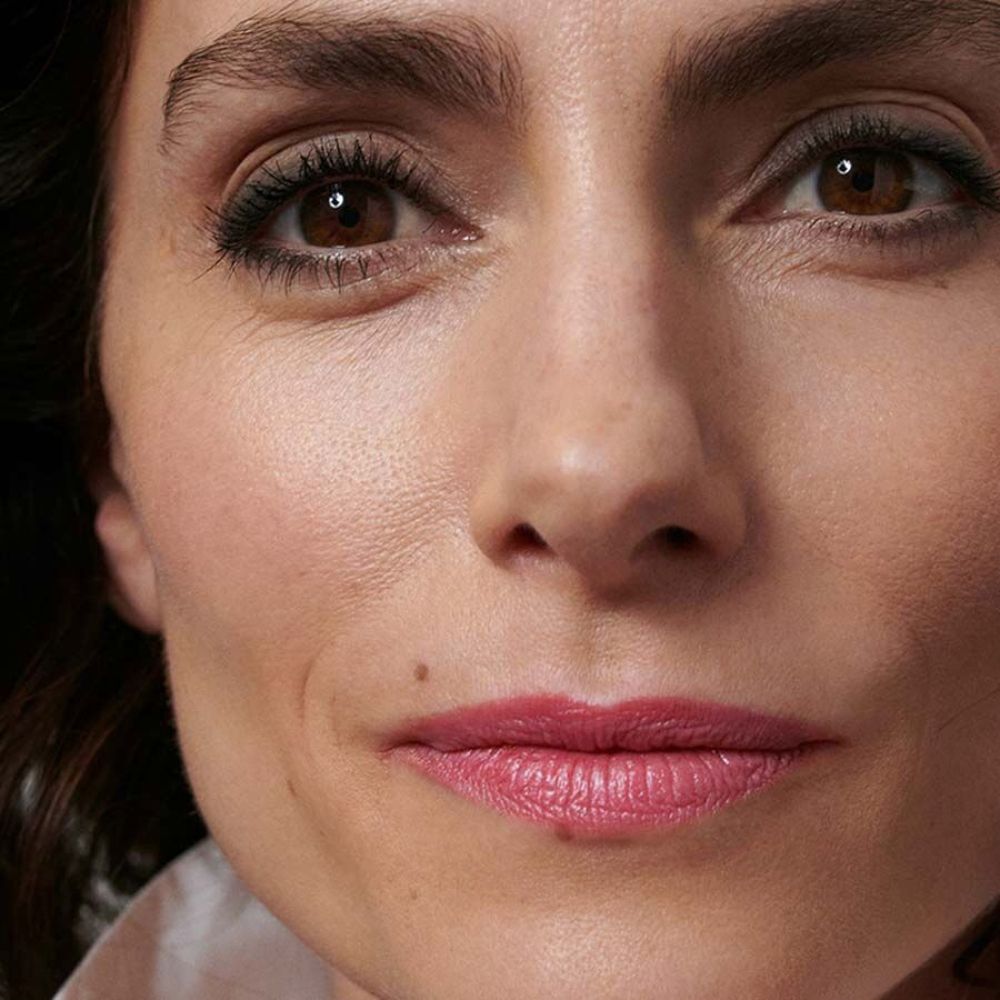 Primo piano di un viso con rossetto rosa. Capelli scuri, occhi marroni.