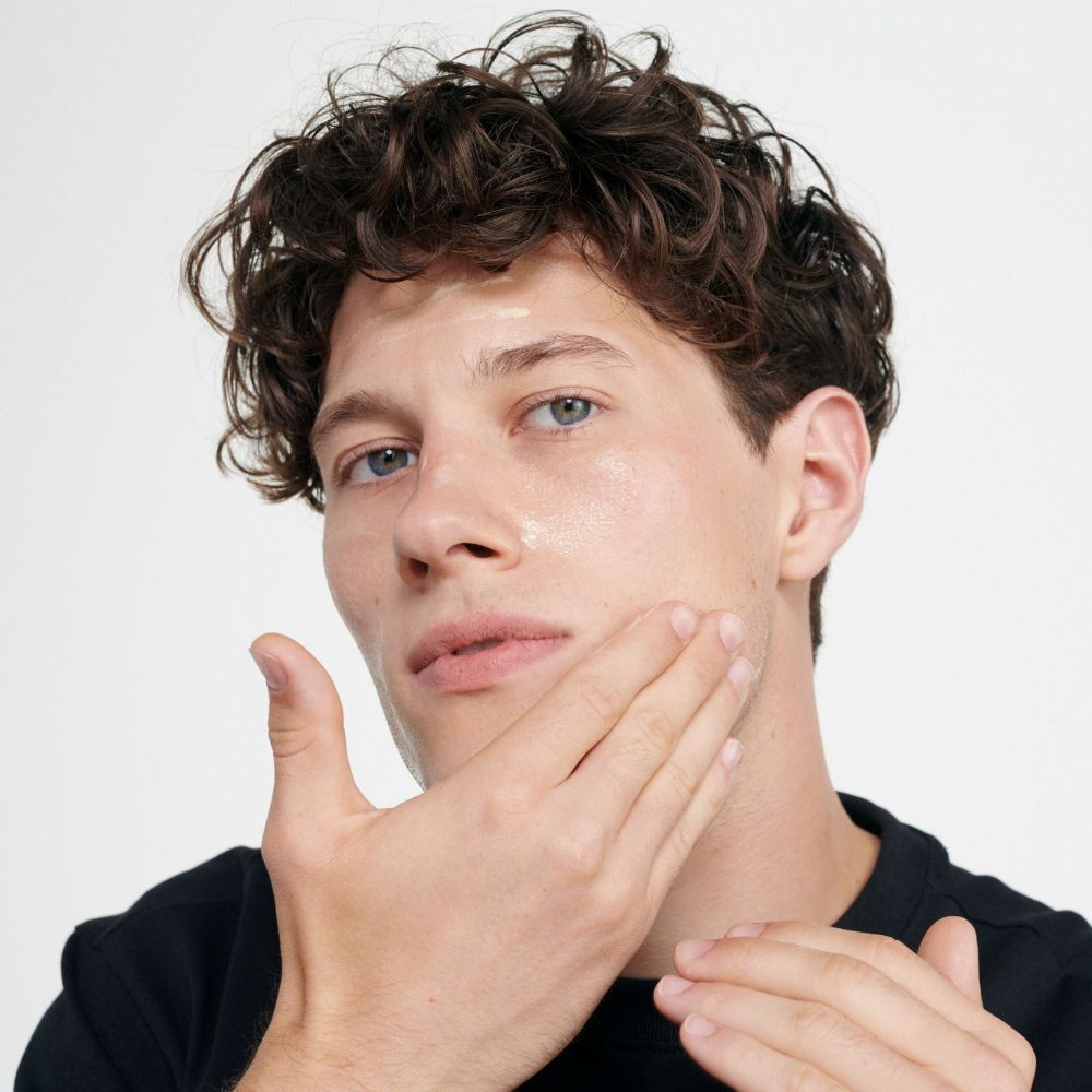 Uomo applica crema sul viso. Pelle chiara, capelli scuri.