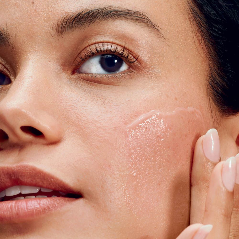 Una donna applica una crema leggera color pesca sulla guancia.