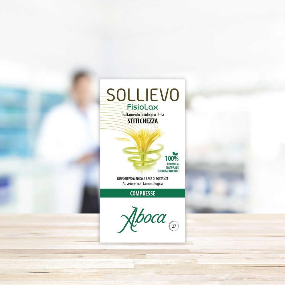 Confezione Sollievo Fisiolax su un tavolo. Etichetta bianca con testo. Marchio: Aboca. Sfondo sfocato.