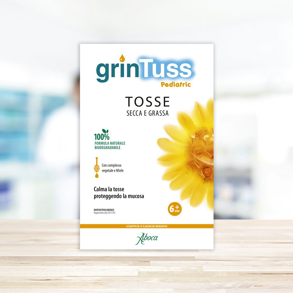 Confezione di Grintuss Pediatric. Logo e nome del prodotto. Fiore giallo. Sfondo sfocato.
