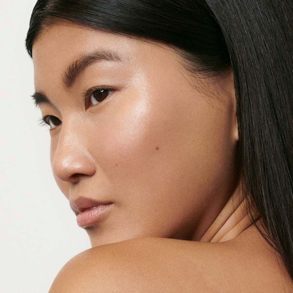 Primo piano di una donna con la pelle luminosa. Viso rivolto di lato. Capelli scuri.