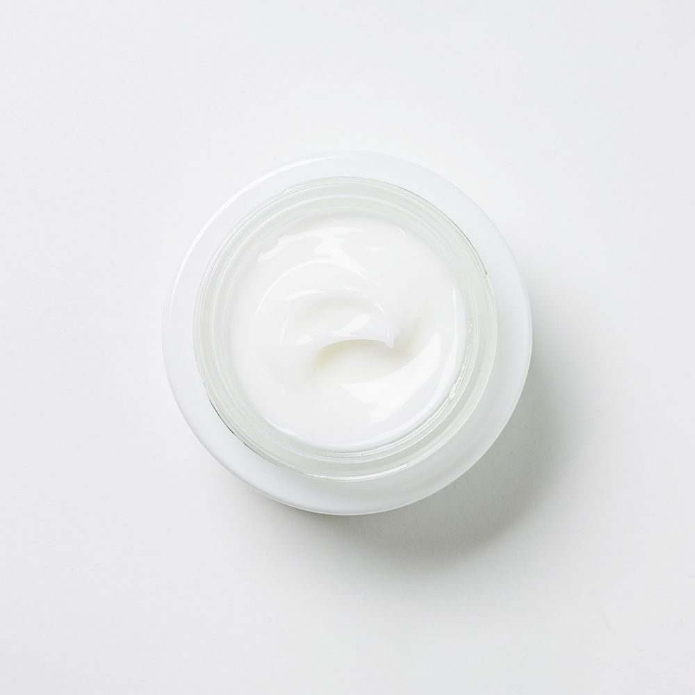 Vista dall'alto di una crema in un contenitore di vetro. La crema è bianca e ha una consistenza liscia.