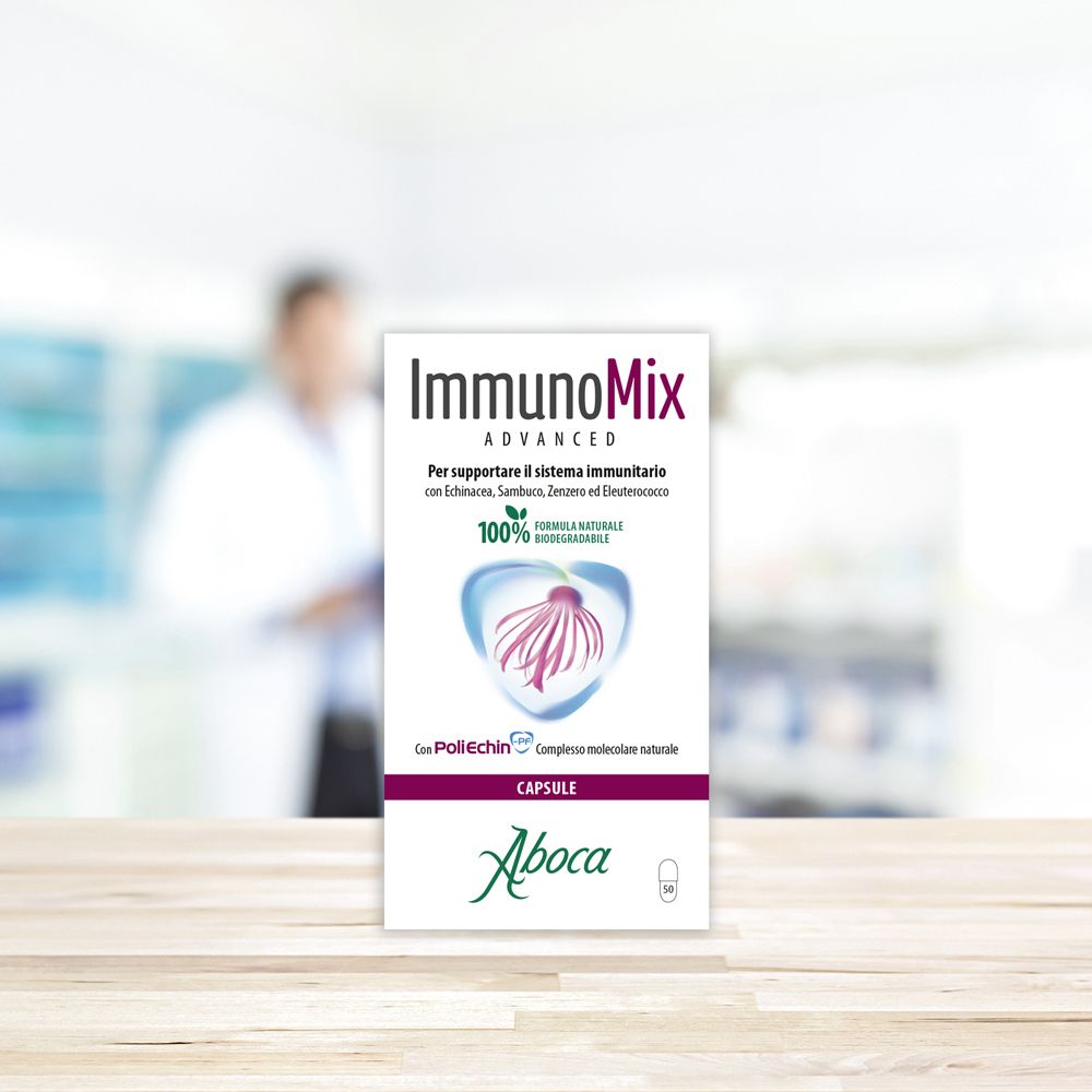 Confezione del prodotto su un tavolo. Testo: Immunomix Advanced, Aboca, 100% biodegradabile. Sfondo: persona sfocata.