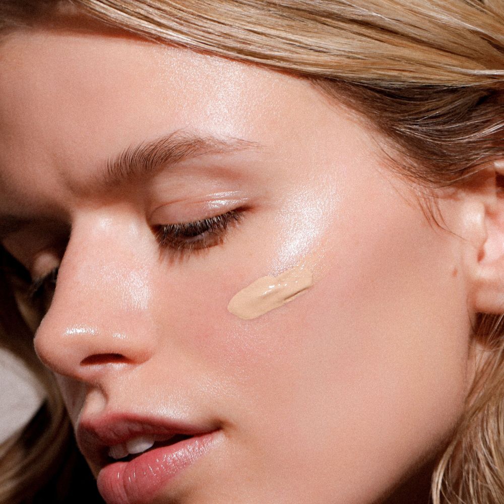 Donna con crema solare colorata sulla guancia. La pelle appare lucida.