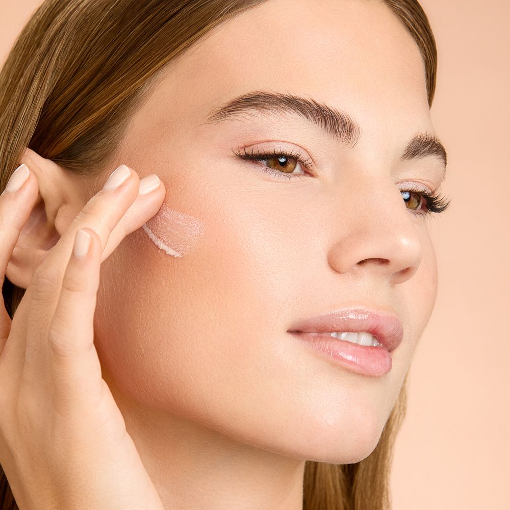 Donna applica il prodotto. Prodotto per la cura della pelle applicato sulla guancia. Sfondo beige.