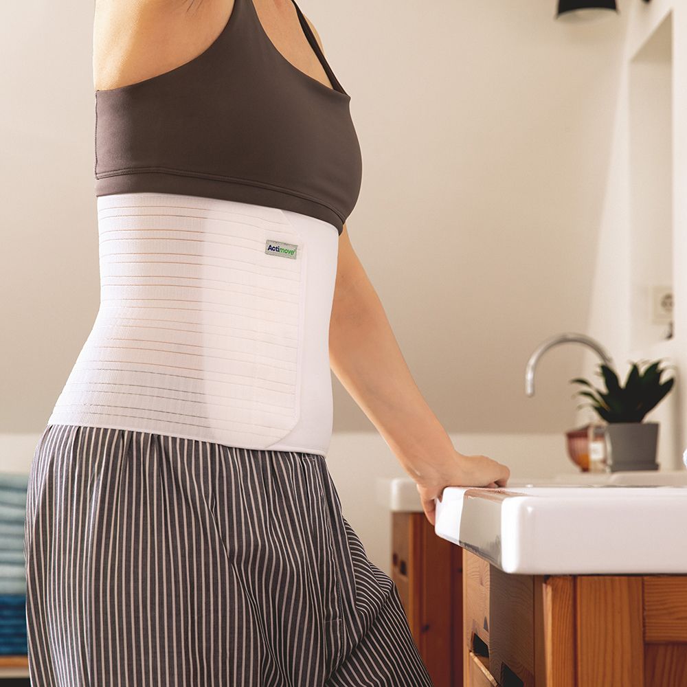 Persona che indossa una fascia addominale Actimove bianca. Strisce verticali. Sfondo bagno.