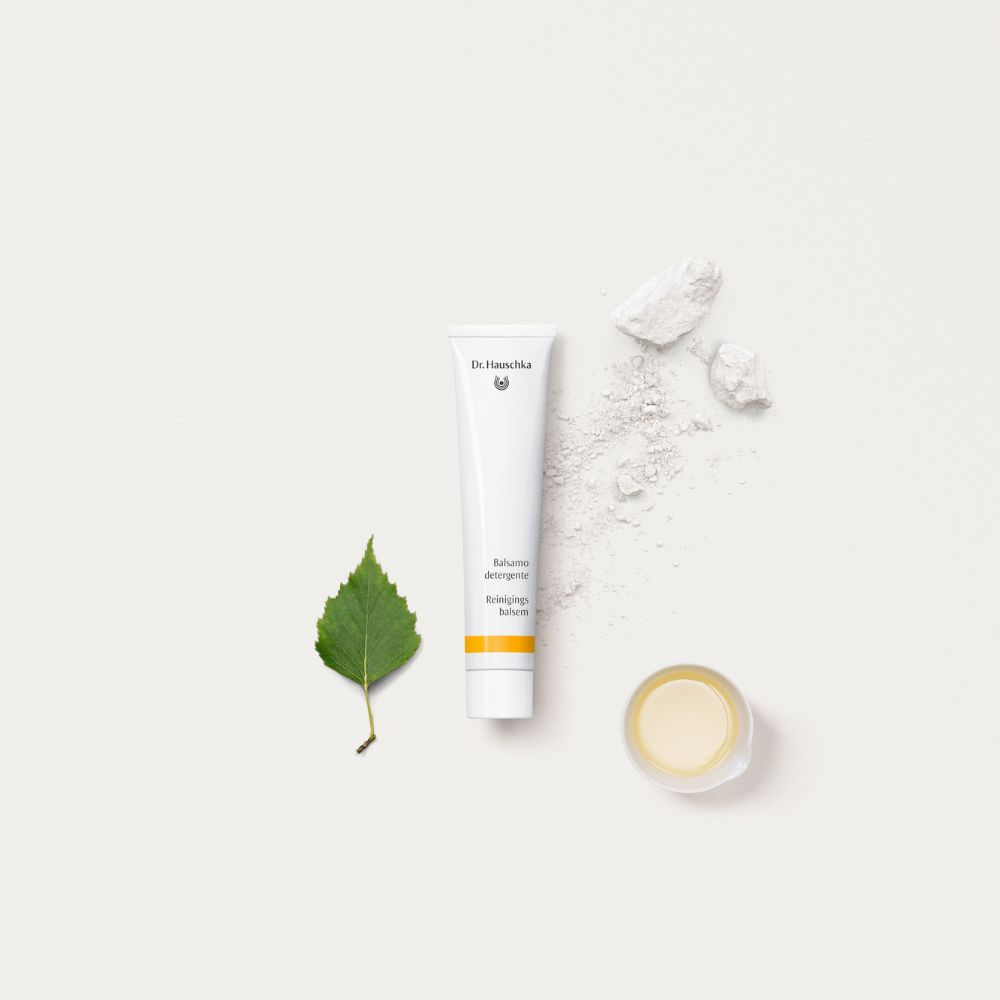 Tubo, foglia e ciotola con polvere bianca. Scritta: Balsamo detergente, Reinigungsbalsam. Marchio Dr. Hauschka.