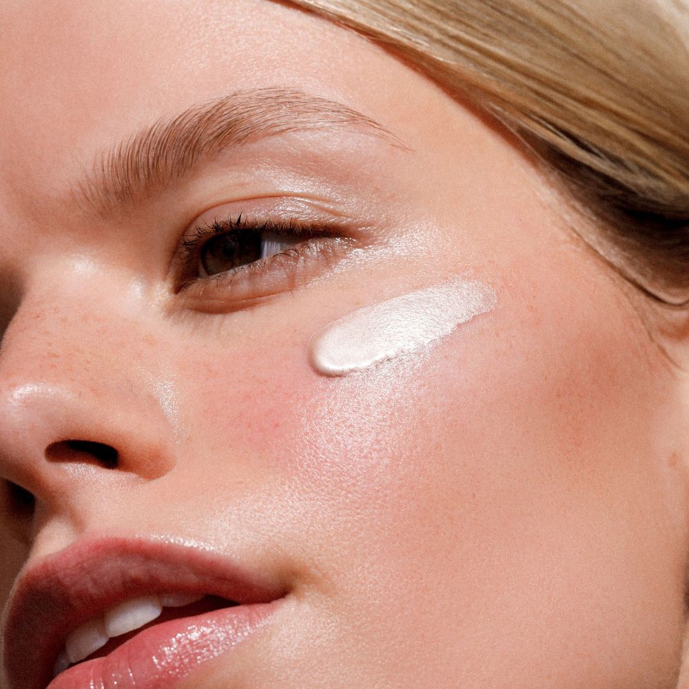 Primo piano di un viso con Illuminating Fluid sulla guancia. La pelle appare lucida.