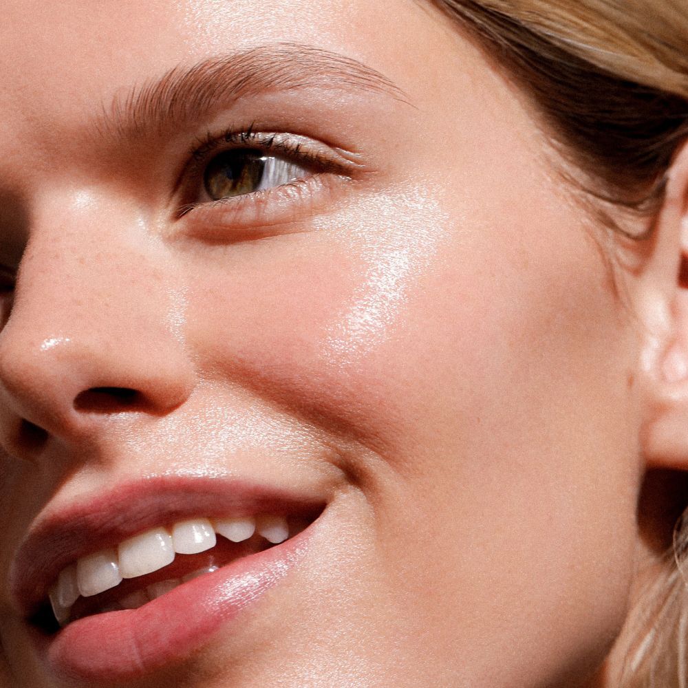 Primo piano di un viso con pelle lucida. Labbra e sopracciglia visibili.