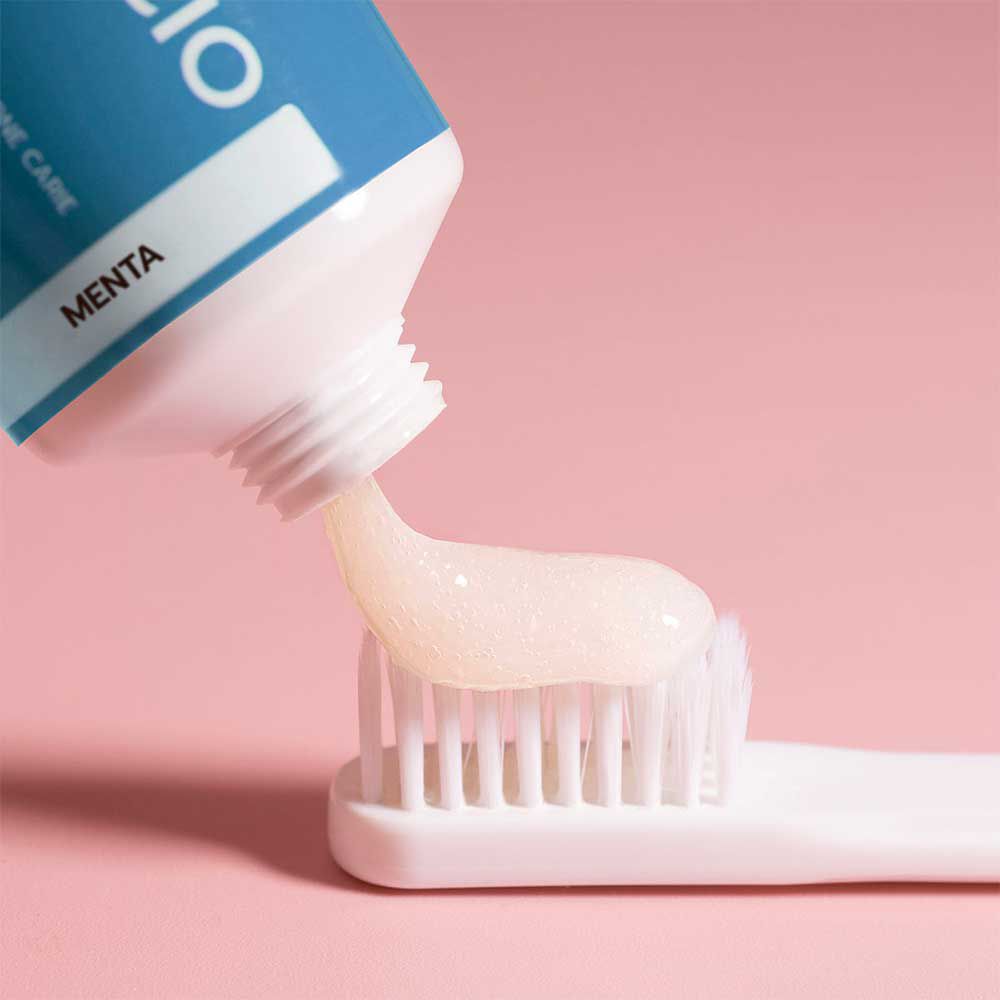 Dentifricio spremuto su uno spazzolino. Sfondo rosa. Tubo con stampa.