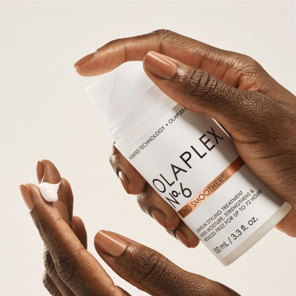 Mani che tengono un flacone bianco. OLAPLEX No.6 Bond Smoother. Prodotto applicato sul dito. Pelle chiara.