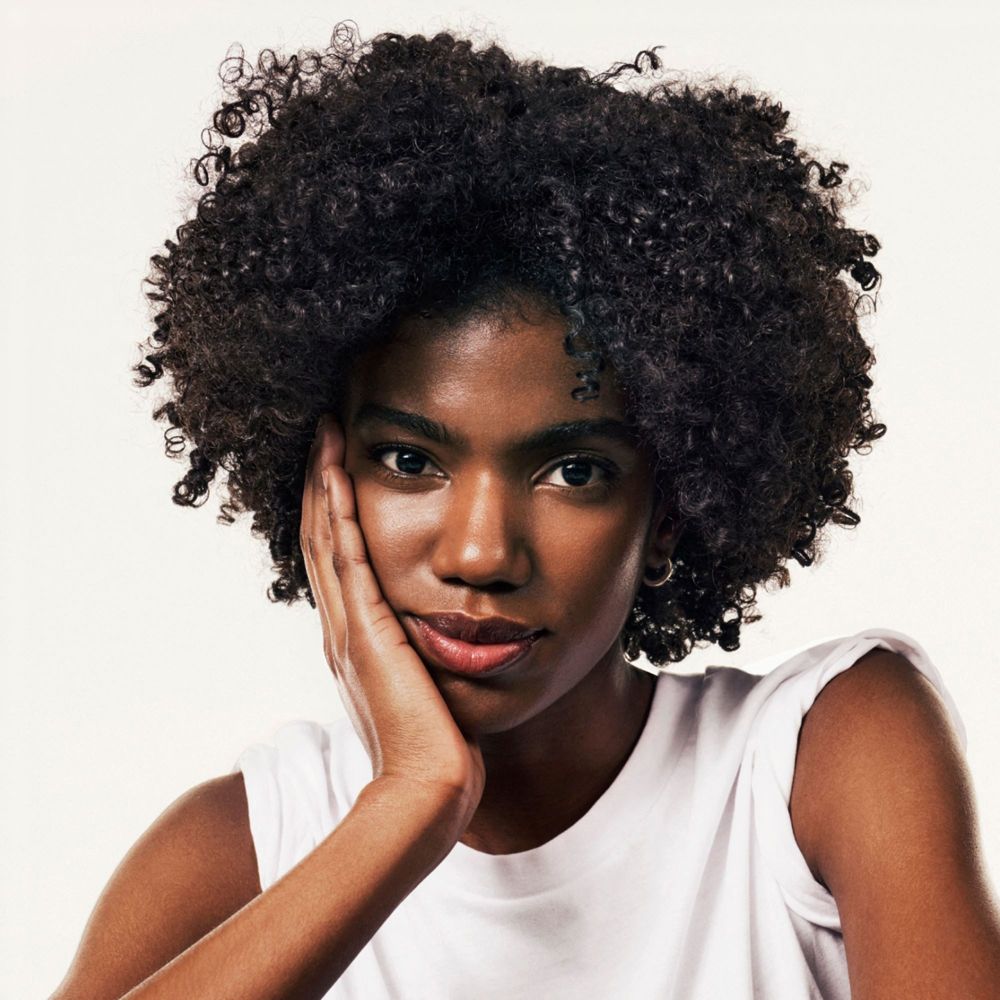 Ritratto di una donna con capelli ricci. Si tocca la guancia con la mano.