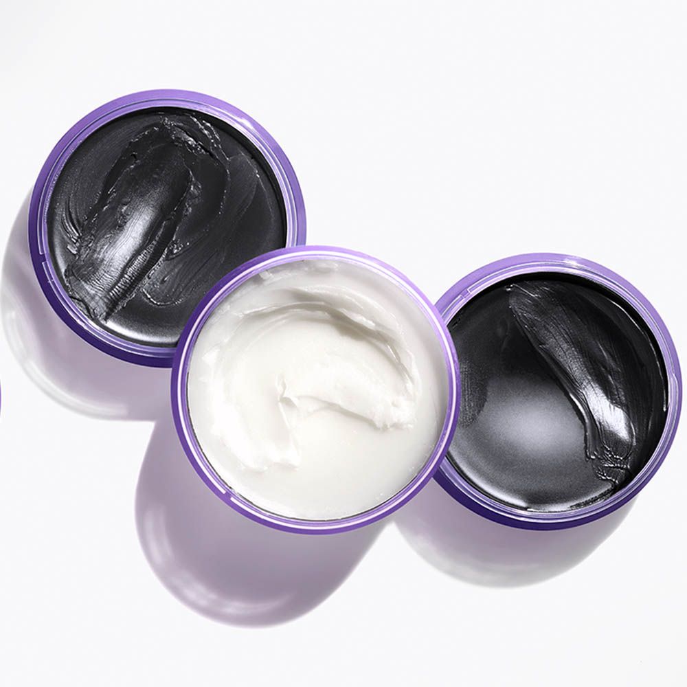Tre barattoli aperti di maschere per il viso: due con maschera al carbone nero, uno con crema bianca.